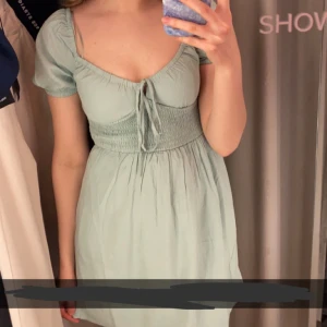 Ljusgrön kort klänning från BikBok - Supersöt ljusgrön kort klänning från BikBok med smockad midja och knyt framtill. Använd ett fåtal gånger då den nu är för liten. Tillverkad i 100% viskos med foder i modal. Perfekt för sommaren och ger en romantisk vibe med sin feminina passform och mjuka tyg. Nypris 399kr.