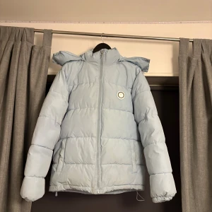 Ljusblå pufferjacka från Trapstar - Säljer en ljusblå pufferjacka från Trapstar med stor logga broderad på ryggen och rund patch på bröstet. Jackan har dragkedja framtill, hög krage och vadderad design som håller dig varm. Perfekt för dig som vill sticka ut med streetwear-vibe. Hör av dig om du har några frågor.
