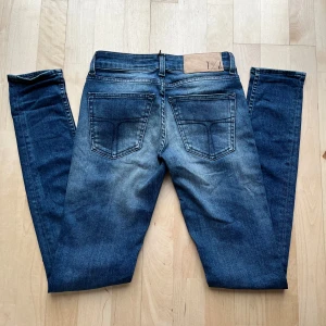 Blå jeans från Tiger of Sweden - Snygga blå jeans från Tiger of Sweden med klassisk femficksdesign och diskret logga på myntfickan. Jeansen har en något tvättad look med ljusare partier och raka ben. Perfekta för dig som gillar stilrena och tidlösa jeans.