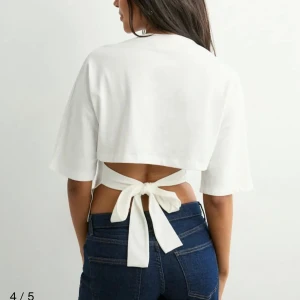 Nelly tröja - Snygg vit croppad topp med halvlånga ärmar och öppen rygg som knyts med en bred rosett. Från Nelly, inga defekter