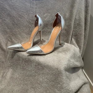 Jättefin silver  klackskor🩶 - Snygga pumps i metallic silver från BEBO med transparenta sidor i syntetmaterial. Skorna har spetsig tå och hög klack som ger en riktigt trendig look. Perfekta för dig som vill sticka ut med en futuristisk vibe. Klacken är smal och elegant.
