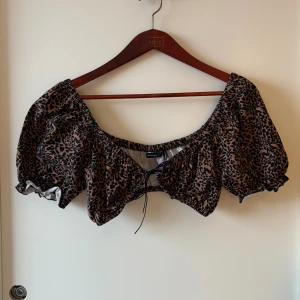 Leopardmönstrad bolerotopp från ASOS - Säljer en brun och svart bolerotopp från ASOS DESIGN med leopardmönster. Toppen har puffiga korta ärmar, snörning framtill och elastisk kant som ger en snygg offshoulder-look. Perfekt för dig som vill sticka ut med coola detaljer och djurprint.