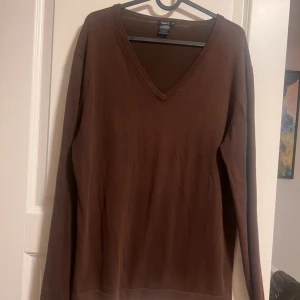 Brun v-ringad tröja Filippa K - Brun v-ringad tröja från Filippa K i storlek M. Tröjan är stickad i mjuk bomull och har långa ärmar med ribbade muddar. Enkel och stilren design som funkar till många olika looks. Perfekt för dig som gillar klassiska och jordnära färger.