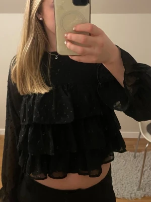 Svart volangblus med glitter - En superfin svart glittrig blus med volanger från Gina Tricot. Den är från Gina Young och i storlek 158/164. Knappt använd. Säljer kjolen från samma sett också. Skriv om du har några frågor!🩷 