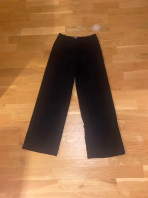 Svarta vida kostymbyxor - Snygga svarta kostymbyxor med hög midja och breda ben. Byxorna har en klassisk look och passar perfekt till en stilren outfit. Tillverkade i ett mjukt material som ger en skön känsla och ett snyggt fall.