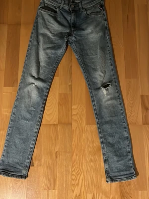 Grå slitna jeans med raka ben - Ett par grå jeans med raka ben och slitningar på båda knäna. Jeansen har klassisk femficksdesign och tydliga sömmar på bakfickorna. Perfekta för en avslappnad och trendig look.