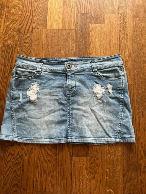 Blå jeanskjol från Only med slitningar - Snygg ljusblå jeanskjol från Only med slitna detaljer framtill, klassisk femficksmodell och hällor för bälte. Kjolen har en kort passform och är perfekt för en avslappnad stil. Skriv för fler bilder!