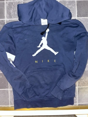 Mörkblå Nike air jordan hoodie  - Mörkblå hoodie från Nike och jordan med stor vit Jordan-logga på bröstet och gul text. Klassisk känguruficka framtill och justerbar huva med svarta snören. Perfekt för en clean och avslappnad stil. (Storlek Small) skick=9/10