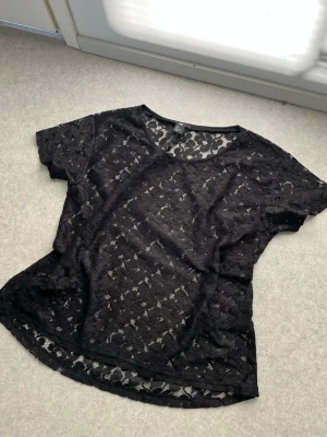 Svart spetsblus från H&M - Säljer en svart blus från H&M i genombruten spets med korta ärmar och rund halsringning. Sparsamt använd och i fint skick!