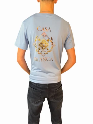 Ljusblå Casa Blanca t-shirt - Ljusblå t-shirt från Casa Blanca med tryckt grafiskt mönster och logga i guld och brunt på både bröstet och ryggen. Klassisk passform med rund hals och korta ärmar. Perfekt för dig som vill sticka ut med stilren design.