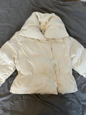 Vit pufferjacka med stor krage - Säljer en riktigt snygg vit pufferjacka med oversized krage och tryckknappar framtill. Jackan har en boxig passform och är perfekt för kyliga dagar. Materialet känns mjukt och puffigt, vilket ger en cool och trendig look.