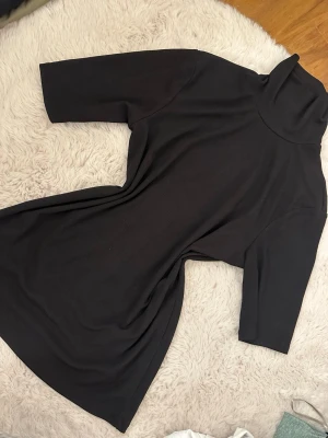 Svart polotröja med halvlånga ärmar - En svart tröja med polokrage och halvlånga ärmar. Tröjan har en enkel, stilren design och är gjord i ett mjukt, stretchigt material som ger en bekväm passform. Perfekt för dig som gillar minimalistisk stil.