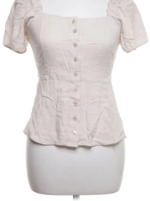 Ljusbeige blus med puffärm och knappar - Supersöt ljusbeige blus i linne- och bomullsblandning med puffiga korta ärmar och knappar hela vägen framtill. Blusen har en lätt figurnära passform och fyrkantig ringning som ger en romantisk vibe. Perfekt till jeans eller kjol.