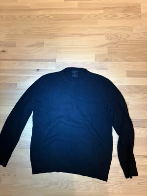 Svart stickad tröja från H&M - En svart stickad tröja från H&M med rund halsringning och ribbade muddar. Tröjan har en enkel, klassisk design och är perfekt för lager-på-lager. Materialet är mjukt och bekvämt, vilket gör den lätt att bära till olika outfits.