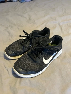 Svarta Nike sneakers med vit sula - Säljer ett par svarta Nike löparskor med vit sula och vit logga på sidan. Skorna har snörning och ovandel i meshmaterial som andas. Perfekta för träning eller vardagsbruk för dig som gillar sportig stil.