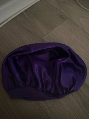 Lila bonnet - Snygg lila sovmössa i glansigt satinmaterial med resårkant. Perfekt för att skydda håret under natten och minska friss. Mössan har en rund form och är mjuk och följsam mot håret. Enkel att använda och ger en lyxig känsla.