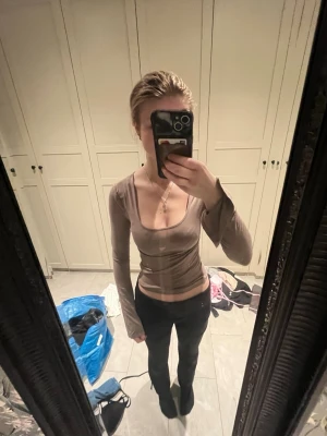 Beige långärmad topp med djup ringning - Trendig beige topp med lång ärm och djup, fyrkantig ringning. Sitter tight och har en croppad passform som framhäver midjan. 