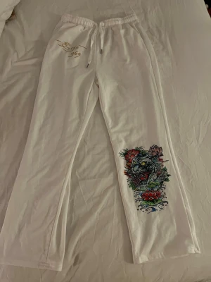 Vita mjukisbyxor med tigertryck - Säljer ett par vita mjukisbyxor från Ed Hardy, köpta secondhand. Byxorna har dock ingen lapp baktill, så om de är äkta eller inte är svårt att bevisa. Ganska tunt material, obs är lite genomskinliga