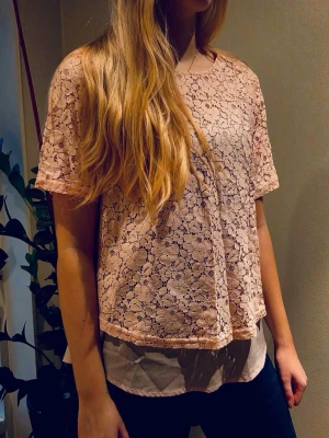 Ljusrosa spetsblus från Cappuccini - Söt ljusrosa blus från Cappuccini i storlek 36. Blusen är tillverkad i ett spetsmaterial med blommigt mönster och har korta ärmar. 