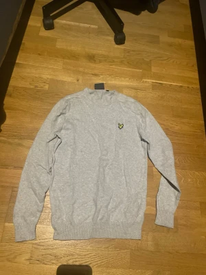 Ljusgrå tröja från Lyle & Scott - Säljer en stilren ljusgrå tröja från Lyle & Scott med deras klassiska gula örnlogga på bröstet. Tröjan har rund halsringning, långa ärmar och ribbade muddar vid ärmslut och nederkant. Perfekt för en clean och avslappnad look. Storlek M. Pris kan diskuteras.