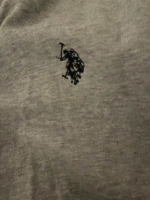 Snygg huvtröja från uss polo - Snygg grå hoodie från U.S. Polo Assn. med dragkedja och justerbar huva. Klassisk logga broderad på bröstet och metallöljetter vid snörningen. Tillverkad i mjukt bomullsmaterial som känns skönt mot huden.