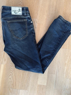 Mörkblå jeans från Jacob Cohen - Snygga mörkblå jeans från Jacob Cohen med klassisk femficksdesign och kontrastsömmar. sopassade för dig som gillar en tidlös look. Materialet är mjukt jeans-tyg i bomull med lite stretch för extra komfort. Notera hål i fickan samt en slitning nere vid gylfen. Size 32. Frågor kom pm, allt gott /Neo💫