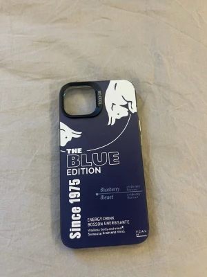 Blått Red Bull-inspirerat mobilskal - till iPhone 13!! Snyggt mobilskal i blått och vitt med Red Bull Blue Edition-energidryckstema. Skalet har tryck med vita tjurar och text, samt öppning för kamera. Tillverkat i tålig plast och passar perfekt för dig som vill sticka ut med din iPhone.