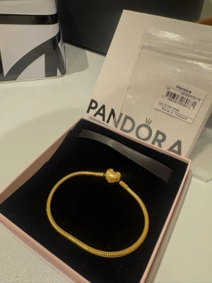 Pandora gulpläterat berlock armband  - Snyggt guldigt armband från Pandora med ett hjärtformat lås. Armbandet har en klassisk ormkedjedesign och kommer i originalask. 18cm! Använd fåtal gånger, säljer pga något för stort så har köpt en storlek mindre. Fick i julklapp så nyinköpt. Finns kvitto
