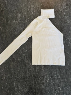 Vit oneshoulder polotopp från Zara - Trendig vit ribbad polotopp från Zara med oneshoulder-design och lång ärm. Toppen är i stretchigt material och har en hög krage som ger en cool och modern look. Perfekt för dig som vill sticka ut med en unik topp.