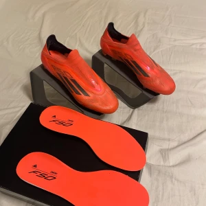 Adidas F50 elite röda fotbollsskor - Snygga röda Adidas F50 elite fotbollsskor med svarta detaljer och låg profil. Skorna har en aerodynamisk form och är tillverkade i syntetmaterial för lätt vikt och snabbhet på planen. Perfekta för dig som vill sticka ut och prestera på topp under matchen. De är använda fåtal gånger under träning och är i mycket bra skick!