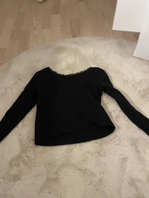 Svart långärmad topp med spetskant - Snygg svart långärmad topp med u-ringning och fin spetskant vid halsen. Modellen är enkel men har en feminin touch tack vare spetsdetaljen. Perfekt att styla med jeans eller kjol för en trendig look.