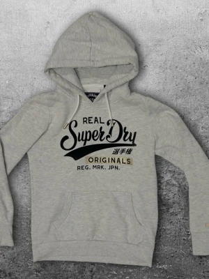 Superdry hoodie XS - En väldigt snygg hoodie från Superdry i storlek XS. Färg vit med guldiga detaljer. Mycket bra skick! 😀