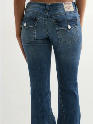 Blå True Religion bootcut jeans - Säljer ett par blå jeans från True Religion med klassiska kontrastsömmar och dekorativa ficklock bak. Modellen har bootcut passform och normal midja. Jeansen är tillverkade i bomull med en snygg tvätt och har detaljer som knappar och fickor både fram och bak. Använda 2 ggr, w28🙃💕 har en liten slitning vid ena hälen kolla bild 6💕