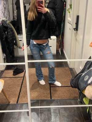 Blå bootcut jeans med slitningar - Säljer ett par blå bootcut jeans med slitna detaljer och låg midja. Jeansen har klassisk femficksdesign och är tillverkade i denim. Perfekta för dig som gillar en avslappnad och trendig look.