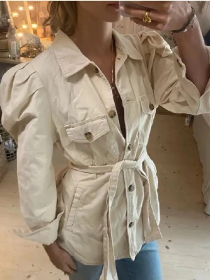 Beige overshirt med puffärm och bälte - Trendig beige overshirt med puffärmar, knappar framtill och två bröstfickor. Jackan har ett knytbart bälte i midjan💕💕. Använd 1 gång 💞ordinarepris 499kr! 