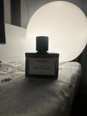 Nõberu Tobacco Vanilla parfym - En stilren parfymflaska från Nõberu med doften Tobacco Vanilla. Flaskan är rektangulär med mörkbrunt glas och svart lock. Etiketten är vit med svart text. Perfekt för dig som gillar varma och kryddiga doftnoter. 45 available.