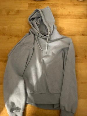 Ljusblå hoodie med huva - Snygg ljusblå hoodie med huva och dragsko. Tröjan har breda muddar vid ärmslut och midja samt en avslappnad passform. Perfekt för en chill och stilren look.
