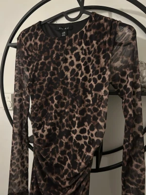 Leopardmönstrad långärmad klänning - Snygg leopardmönstrad klänning med lång ärm och figurnära passform. Klänningen har rund halsringning och är tillverkad i ett stretchigt syntetmaterial som ger en cool look. Perfekt för dig som vill sticka ut med ett djurmönster.
