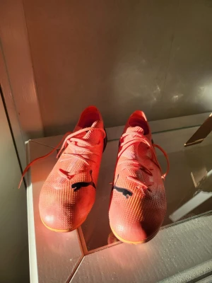 Puma orange fotbollsskor med snörning - Säljer ett par snygga orangea fotbollsskor från Puma med svart logga på ovansidan. Skorna har snörning och är tillverkade i ett lätt syntetmaterial för bra bollkontroll. Yttersulan har dobbar för optimalt grepp på planen. Perfekta för dig som vill sticka ut på matchen! Passar för barn som 33 eller 34 i storlek