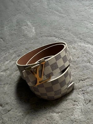 Snygg bälte  - Snyggt bälte i Damier Azur-mönster med beige och gråa rutor,  och är gjort i canvas med läderdetaljer. Perfekt accessoar för att lyfta din outfit med en lyxig touch.