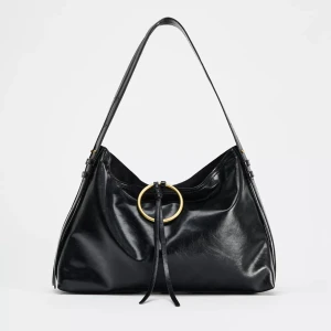 Svart väska Zara - Stilren svart handväska med en guldfärgad metallring framtill (supersnygg detalj). Väskan har en mjuk och slouchy form. Perfekt för både vardag och fest. Köpt för 2 år sedan därav slutsåld. Har endast använt den 1 gång så den är i mycket bra skick.