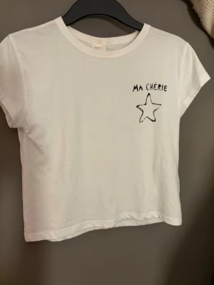 Vit ’ma Chérie’ t-shirt från Gina Tricot - Vit t-shirt med svart tryck 'Ma Chérie' från Gina Tricot.