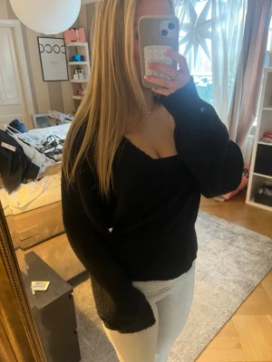 Svart stickad omlott tröja med v-ringning - Mysig svart stickad omlott tröja med djup v-ringning och långa ärmar. Tröjan har en avslappnad passform och är perfekt att matcha med jeans eller kjol. 