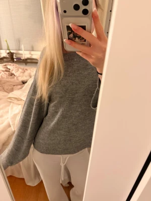 Grå basic stickad tröja - Mysig grå stickad tröja med rund hals och avslappnad passform. Perfekt för lager-på-lager och enkel att matcha med olika outfits. Tröjan har långa ärmar och är tillverkad i ett mjukt material som känns skönt mot huden.