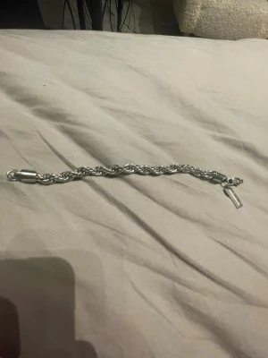 Flätat silverfärgat armband - Snyggt armband i silverfärgad metall med flätad kedja och ett rektangulärt hänge med ingraverad text 'JH 13'. Armbandet har ett robust lås och passar perfekt för dig som gillar stilrena accessoarer.