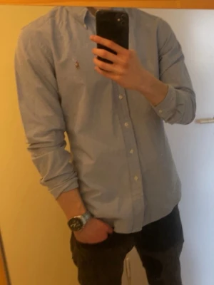 Ljusblå skjorta från Ralph Lauren - Klassisk ljusblå skjorta från Ralph Lauren med knappslå framtill och den ikoniska broderade loggan på bröstet. Perfekt för en clean och stilren look.  Nypris ligger på runt 1600 Den är i nyskick och har inga defekter 😄 Priset är inte hugget i sten 🤙