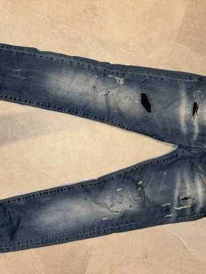 Blå slitna jeans från Dsquared2 - Snygga blå jeans från Dsquared2 med slitningar och hål på framsidan för en cool, trendig look. Jeansen har klassisk femficksdesign, tydlig Dsquared2-patch bak och är tillverkade i bomull. Perfekta för dig som gillar streetstyle.