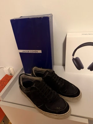 Svarta sneakers från Jacob Cohén - Svarta sneakers från Jacob Cohén med vit sula och klassisk snörning. Skorna har en låg profil och är tillverkade i skinn med diskreta sömdetaljer. Perfekta för en stilren och avslappnad look.