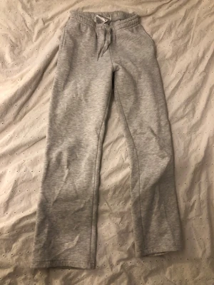 Grå mjukisbyxor med snörning - Mysiga grå mjukisbyxor med rak passform och snörning i midjan. Tillverkade i mjukt bomullsmaterial och har resår i midjan för extra komfort. Perfekta för chill dagar hemma eller när du vill vara bekväm.