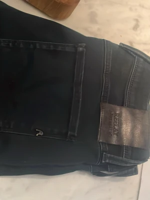 Svarta Replay jeans med skinnpatch - Svarta jeans från Replay med klassisk femficksdesign och svart skinnpatch med logga bak i midjan. Snygg tvätt och raka ben, perfekta till din vardagsstil.